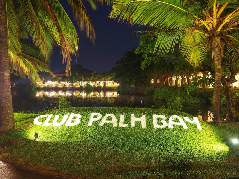 Illuminated 'CLUB PALM BAY' sign between palm trees at night