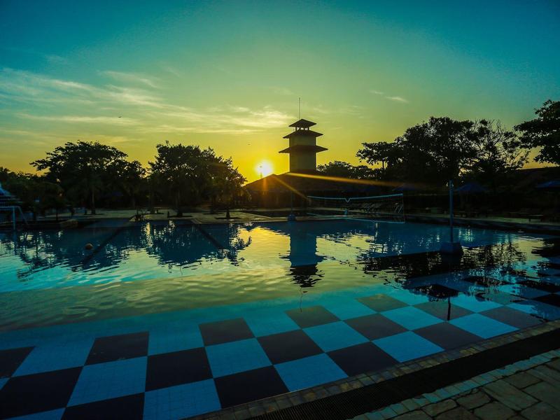 Sunset over a pool with reflective water and a tower in the background.