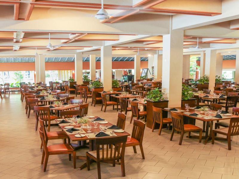Large, bright dining room with wooden tables, chairs, and set tables.