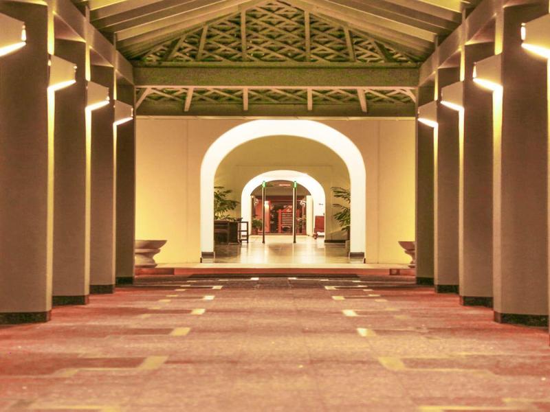 View through a long covered colonnade with lighting and carpeted floor.