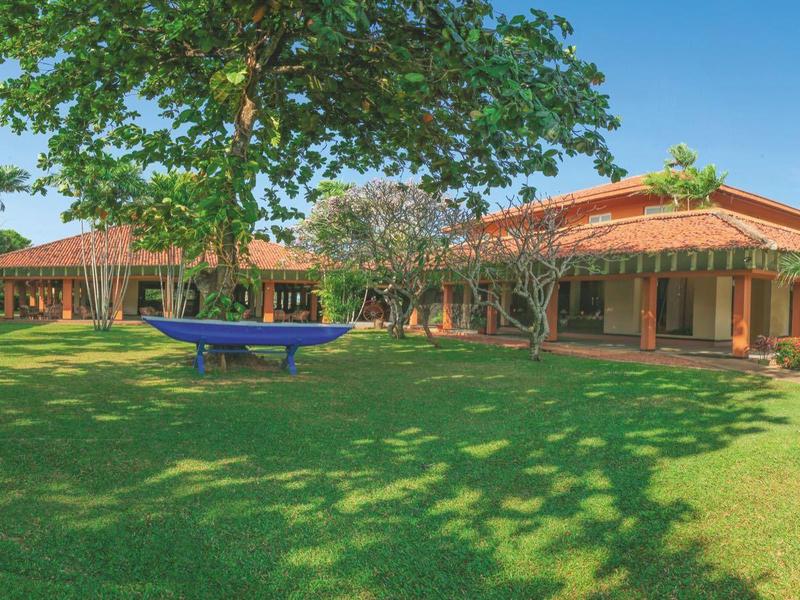 Large hotel with spacious garden and trees under clear sky.