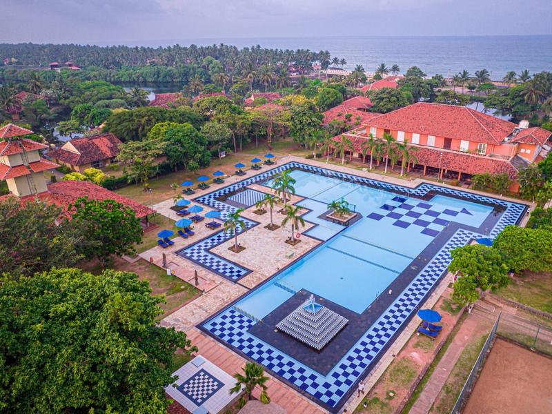 Large outdoor pool with blue loungers surrounded by tropical greenery near the coast.