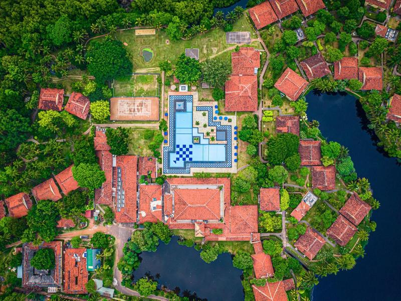 Aerial view of a resort with a pool in the center, surrounded by trees, buildings, and lakes.