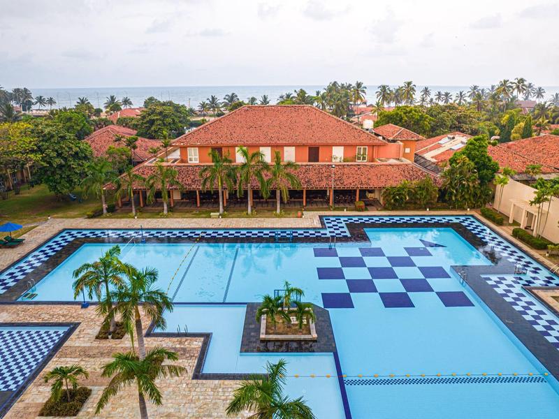 Large pool with blue checkerboard pattern, surrounded by palm trees and red rooftops.