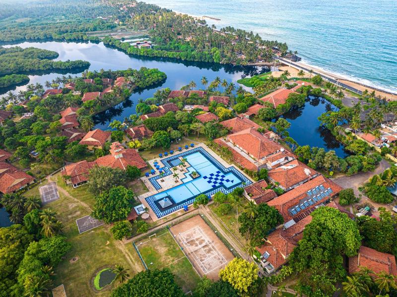 Aerial view of a resort with pool, green areas, and beach near the sea.