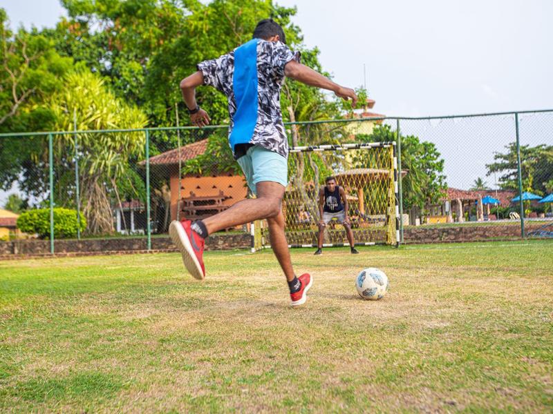Boy playing soccer outdoors on a field in front of a goal.