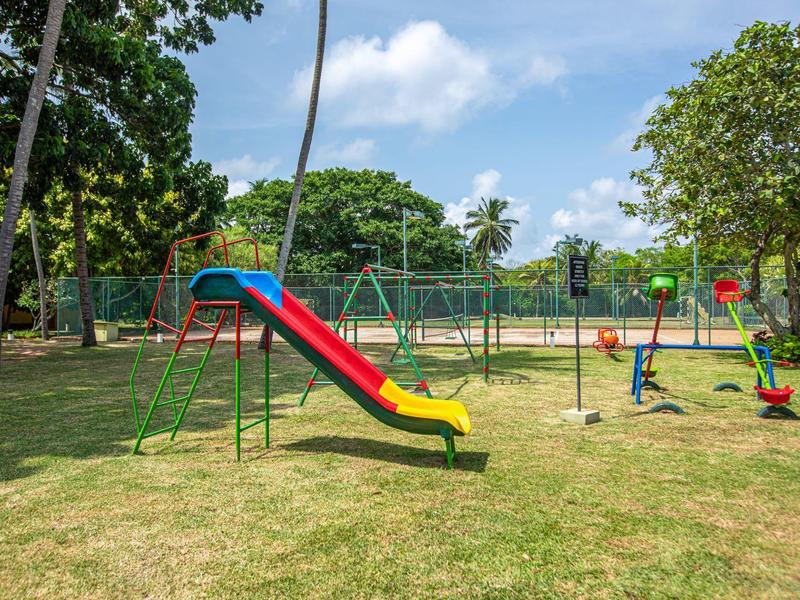 Children's playground with colorful slide and swings on grassy area under blue sky.