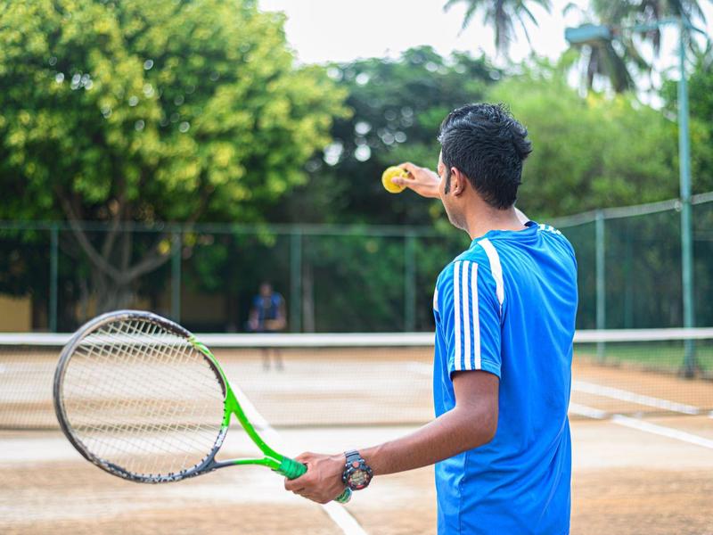 A man in a blue jersey on a tennis court holds a racket and tosses a ball in the air.