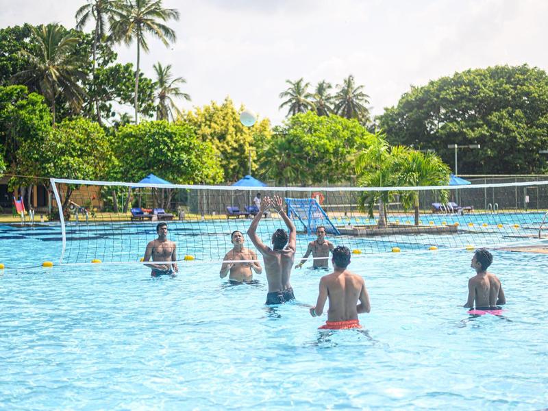 People playing volleyball in an outdoor pool with trees in the background.