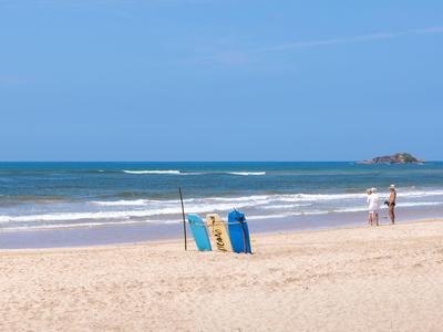 Strand mit hellem Sand, blauem Meer und wenigen Menschen im Hintergrund bei klarem Himmel.