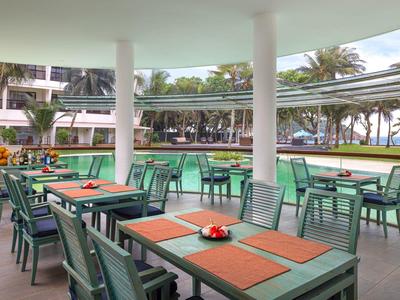 Außenrestaurant mit grünen Stühlen, Tischen, Pool und Palmen im Hintergrund.