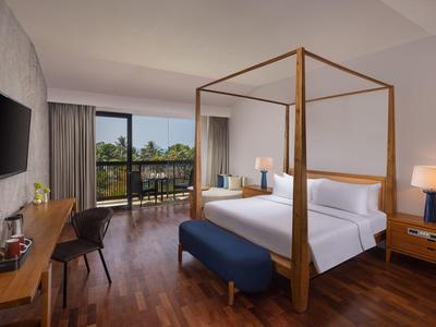 Helles Hotelzimmer mit Holzboden, Himmelbett, Schreibtisch, Fernseher und Balkon mit Blick ins Grüne.