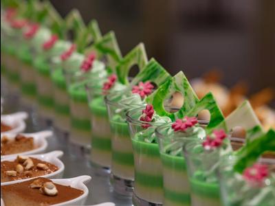 Reihe von gläsernen Dessertbechern mit grünem Schaum und Schokoladenstücken, unscharfer Hintergrund.