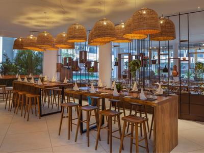 Modernes Restaurant mit Holztischen, Stühlen und großen geflochtenen Lampenschirmen.