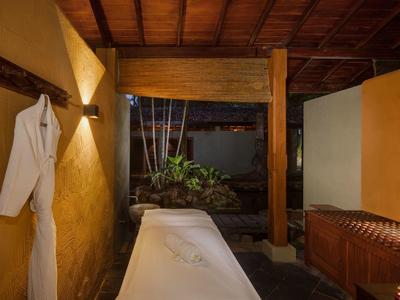 Gemütlicher Massageraum mit Holzdecke, gelben Wänden, Massagetisch und Bademantel an der Wand.