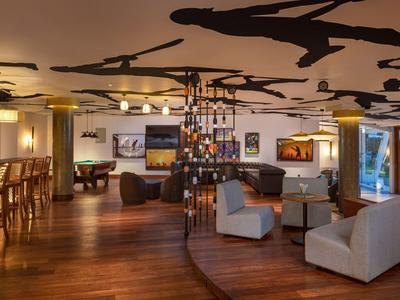 Moderne Lounge mit Holzboden, stilvollen Sesseln, Barbereich und dekorativen Deckenfiguren.