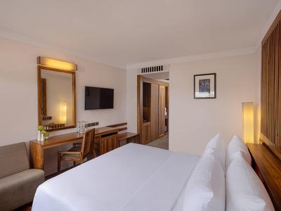 Helles Hotelzimmer mit großem Bett, Holzvertäfelung, Schreibtisch, Fernseher und gemütlichem Sessel.