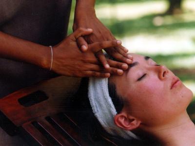 Person entspannt mit geschlossenen Augen, während Hände behutsam Stirn und Kopf massieren.