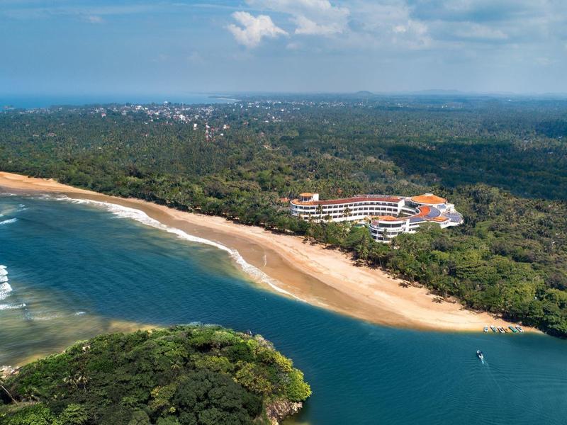 Küstenlandschaft mit Strand, bewaldetem Ufer und Gebäuden nahe Meer und Flussmündung.