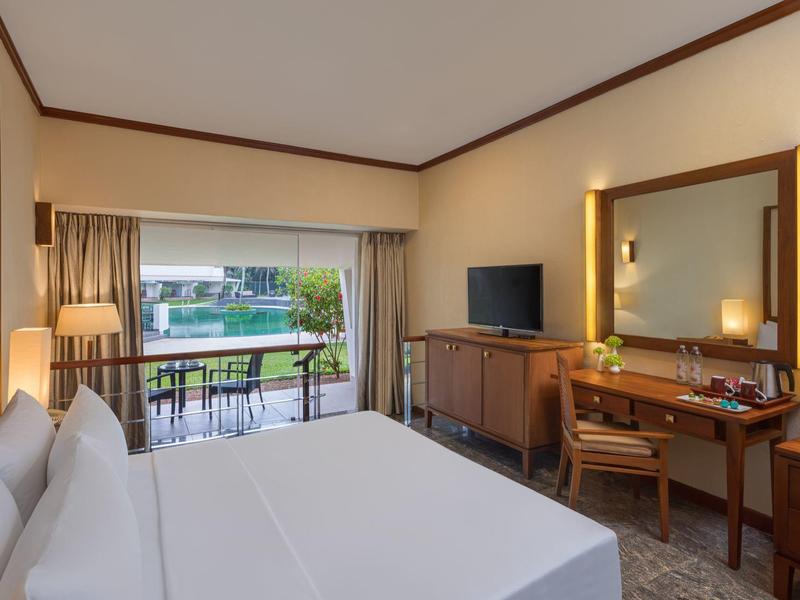 Modernes Hotelzimmer mit großem Bett, Schreibtisch, Fernseher und Blick auf Terrasse mit Pool.