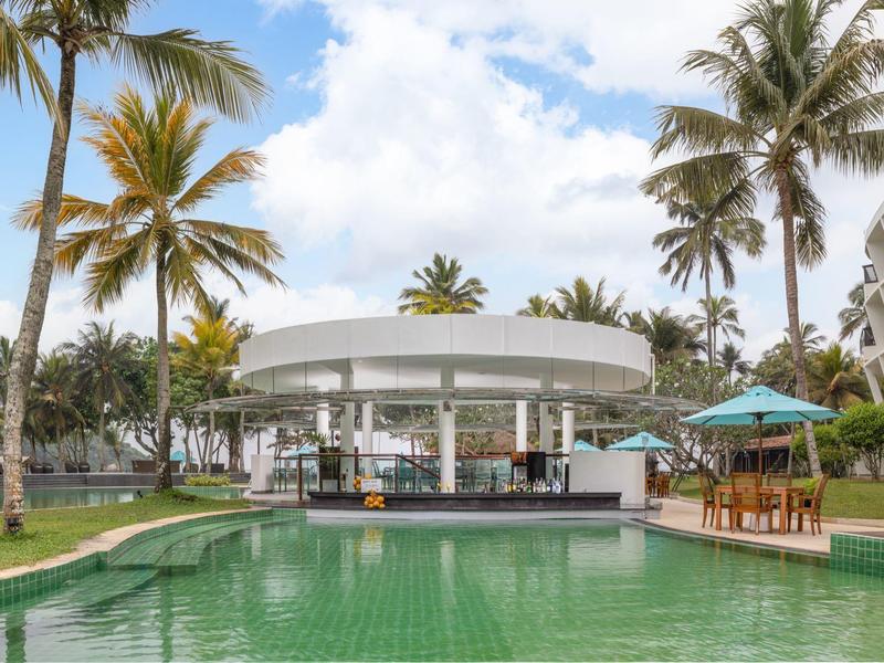 Moderner Poolbereich mit Bar, grünes Wasser, Palmen und blauer Himmel im tropischen Ambiente.