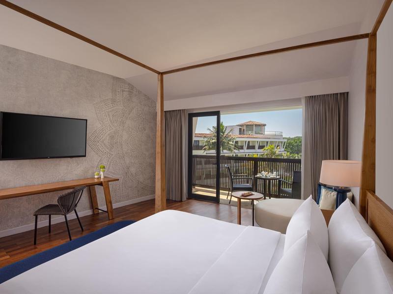 Modernes Schlafzimmer mit großem Bett, TV an der Wand und Balkon mit Blick auf Nachbargebäude.