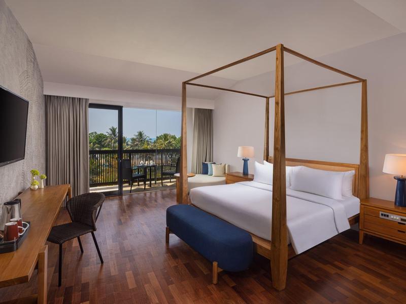 Helles Hotelzimmer mit Holzboden, Himmelbett, Schreibtisch, Fernseher und Balkon mit Blick ins Grüne.