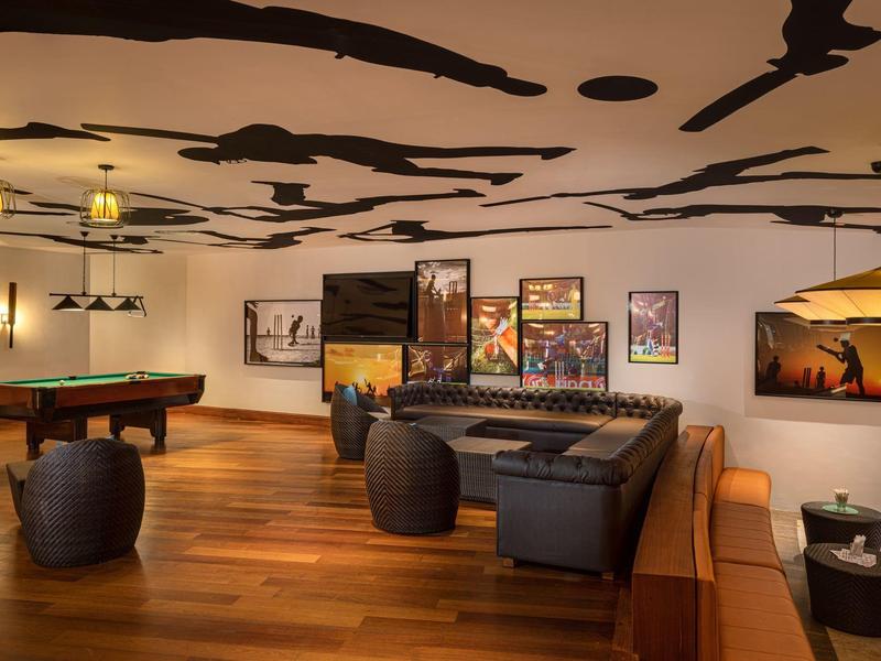 Großer Raum mit Holzboden, Billardtisch, Ledersofas und stilvollen Lampen an weißer Decke.