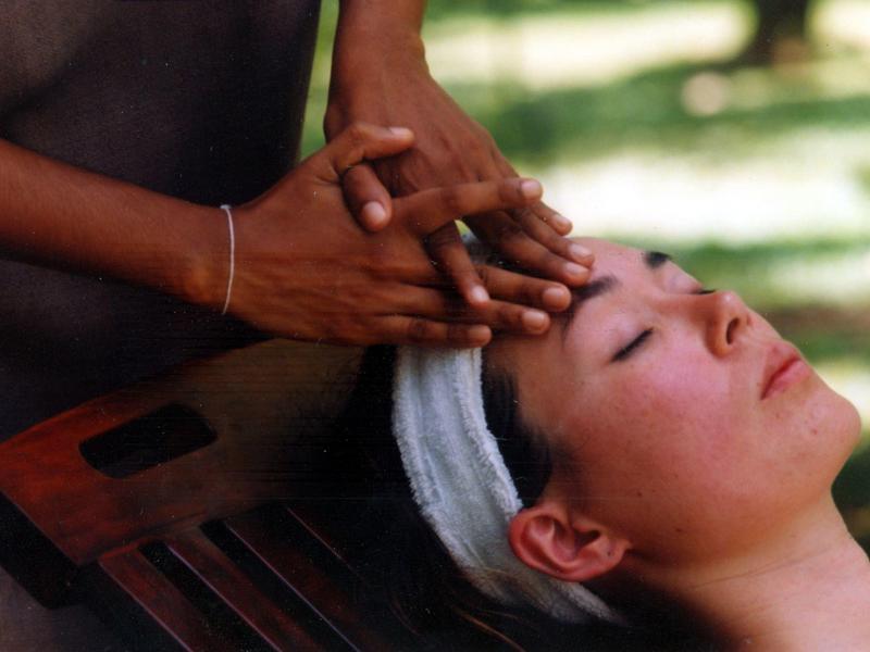 Person entspannt mit geschlossenen Augen, während Hände behutsam Stirn und Kopf massieren.