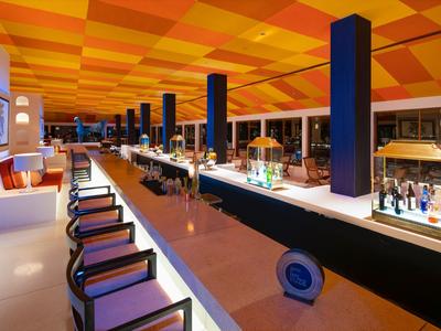 Moderner Hotelbarbereich mit buntem Deckendekor und langen Sitzgelegenheiten.