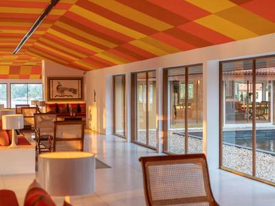 Heller Hotelraum mit großen Fenstern und orange-gelb gestreiftem Deckenmuster.