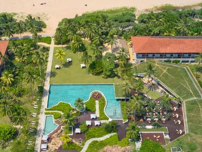 Luftaufnahme eines Hotels mit Pool, grünen Gärten und Strandblick.