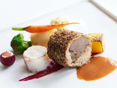 Ein kunstvoll angerichtetes Gericht mit Fleisch, Gemüse und Sauce auf weißem Teller.