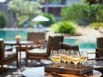 Weingläser auf einem Holztisch vor Außenstühlen in einem sonnigen Hotelgarten mit Pool.