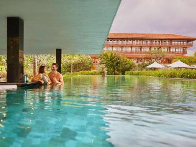 Zwei Personen entspannen im beheizten Außenpool eines Hotels mit moderner Architektur im Hintergrund.