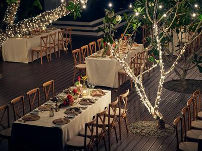 Abendliche Terrasse eines Hotels mit gedeckten Tischen und Bäumen, die mit Lichterketten geschmückt sind.