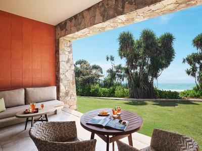 Terrasse mit Sitzbereich, Blick auf Garten und Meer bei klarem Himmel.