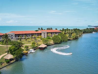 Ein Hotel am Ufer mit Palmengesäumtem Strand und Wassersportmöglichkeiten bei klarem Himmel.