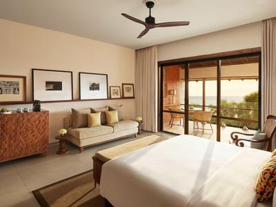 Helles Hotelzimmer mit großem Bett, Sofa, Deckenventilator und Terrasse mit Blick auf die Natur.