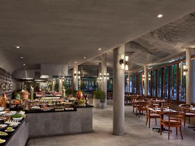 Moderner, offener Restaurantbereich mit Betonwänden, Säulen und Holztischen in einem Hotel.