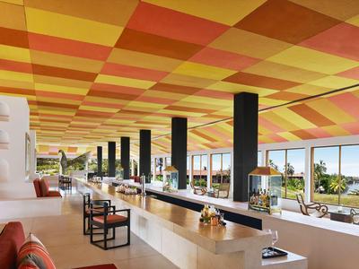 Modernes Hotelrestaurant mit langem weißen Tresen, buntem Deckenmuster und Meerblick.