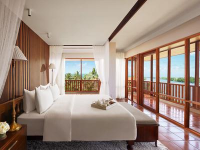 Habitación de hotel luminosa con cama doble y acceso a balcón con vista al paisaje verde.