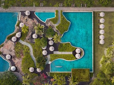 Vista aérea de una piscina de hotel con isla y caminos, rodeada de vegetación verde.