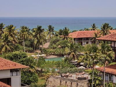 Hotel tropical con techos rojos, rodeado de palmeras y vista al mar.