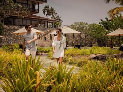 Dos personas ríen mientras caminan por un sendero en un jardín tropical de un resort.