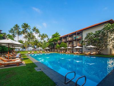 Hotelpool mit Liegestühlen, Sonnenschirmen und Palmen unter blauem Himmel