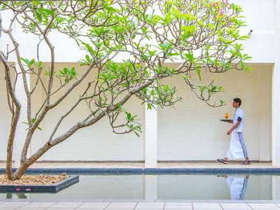 Ein Mann in traditioneller Kleidung geht an einem Baum entlang eines Wasserbeckens in einem modernen, hellen Innenhof.