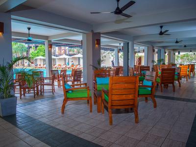 Otwarta jadalnia z drewnianymi stołami i krzesłami, z widokiem na basen na zewnątrz.