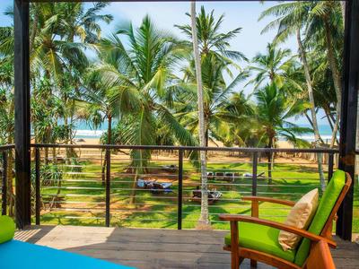 Balkon z krzesłami z widokiem na palmy, trawiasty teren i plażę w tle.