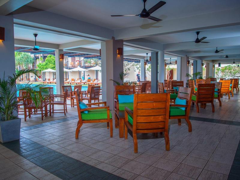 Otwarta jadalnia z drewnianymi stołami i krzesłami, z widokiem na basen na zewnątrz.